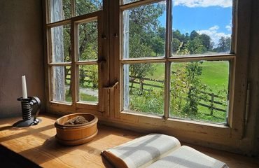 Ventana abierta de madera con vistas a un paisaje verde y luminoso, un libro abierto y una vela encendida, imagen del artículo sobre cómo afrontar los cambios de la vida de Jose Manuel Aguilar.